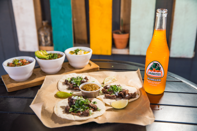 Three tacos with an orange soda on a table.